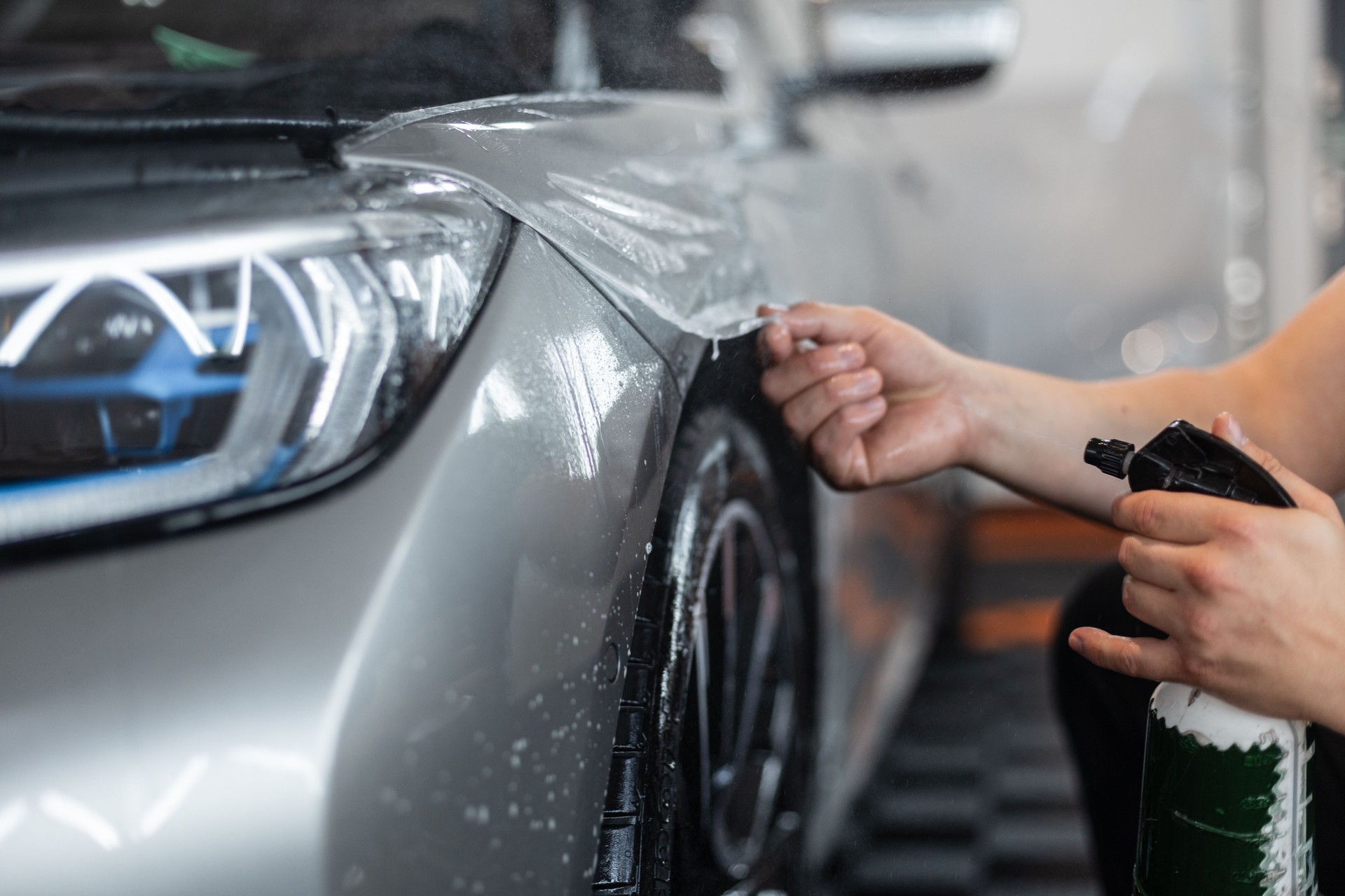 Professional man covers a car with protective film in a detailing center. Car protection and care